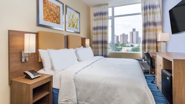 A hotel room with a large bed, a desk, a chair, a TV, and a window with curtains.