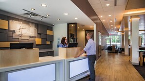 A hotel reception area with a modern design, featuring a reception desk, a digital screen, and a wooden floor.