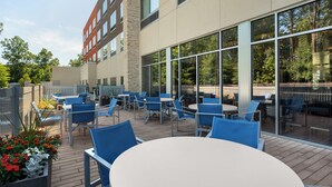 An outdoor patio with tables and chairs, large windows, and a stone wall.