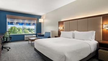 A hotel room with a large bed, a desk, a chair, and a window with a view of trees.