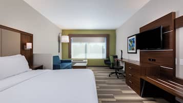 A hotel room with a large bed, a desk with a chair, a television, and a window with blinds.