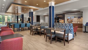 A modern restaurant with wooden tables and chairs, a bar area, and a patterned booth seating.
