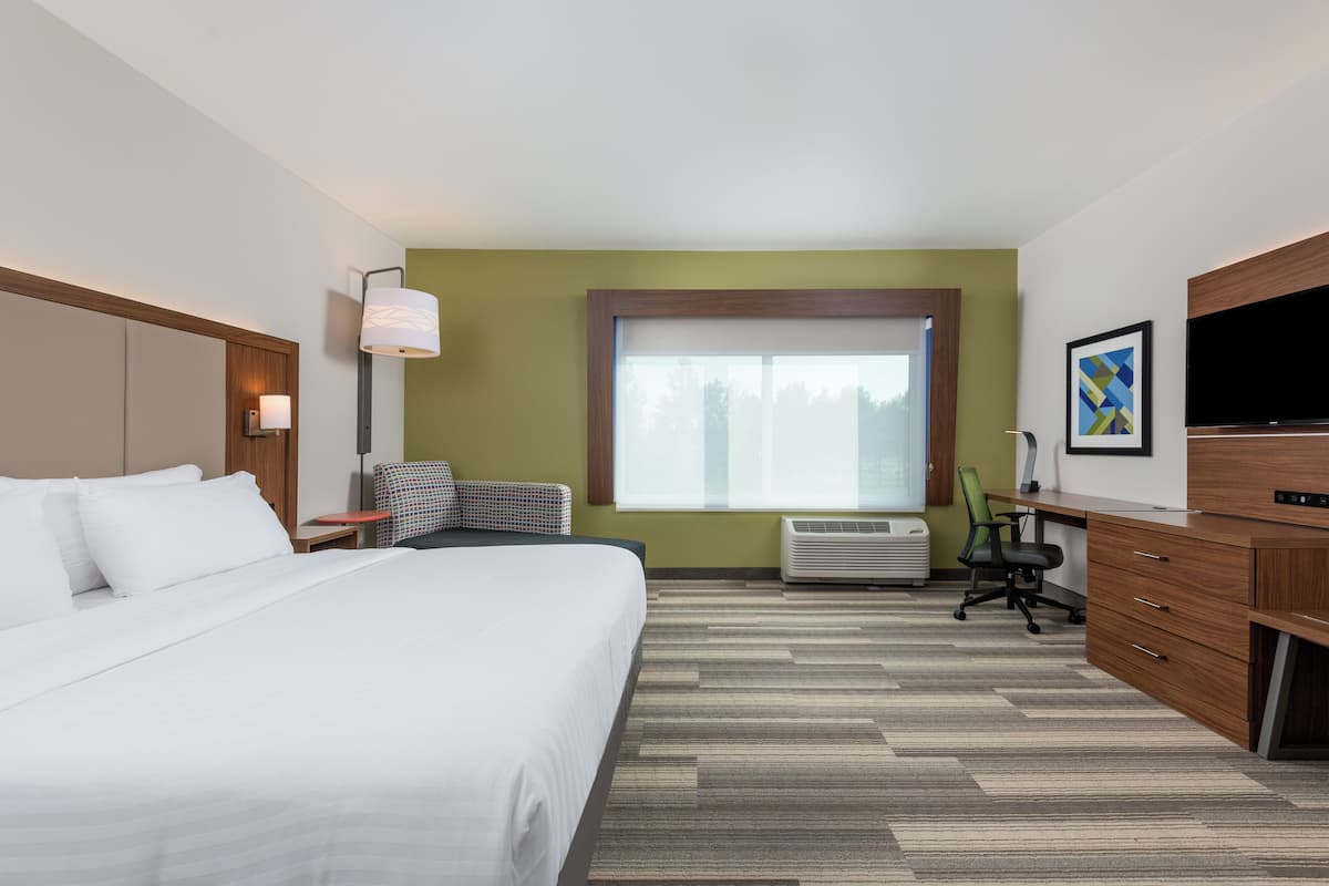 Une chambre d’hôtel avec un grand lit, un bureau, une chaise, un climatiseur et une télévision.