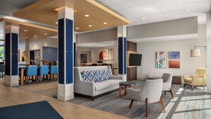 A modern hotel lobby with a seating area, a bar, and a kitchen in the background.