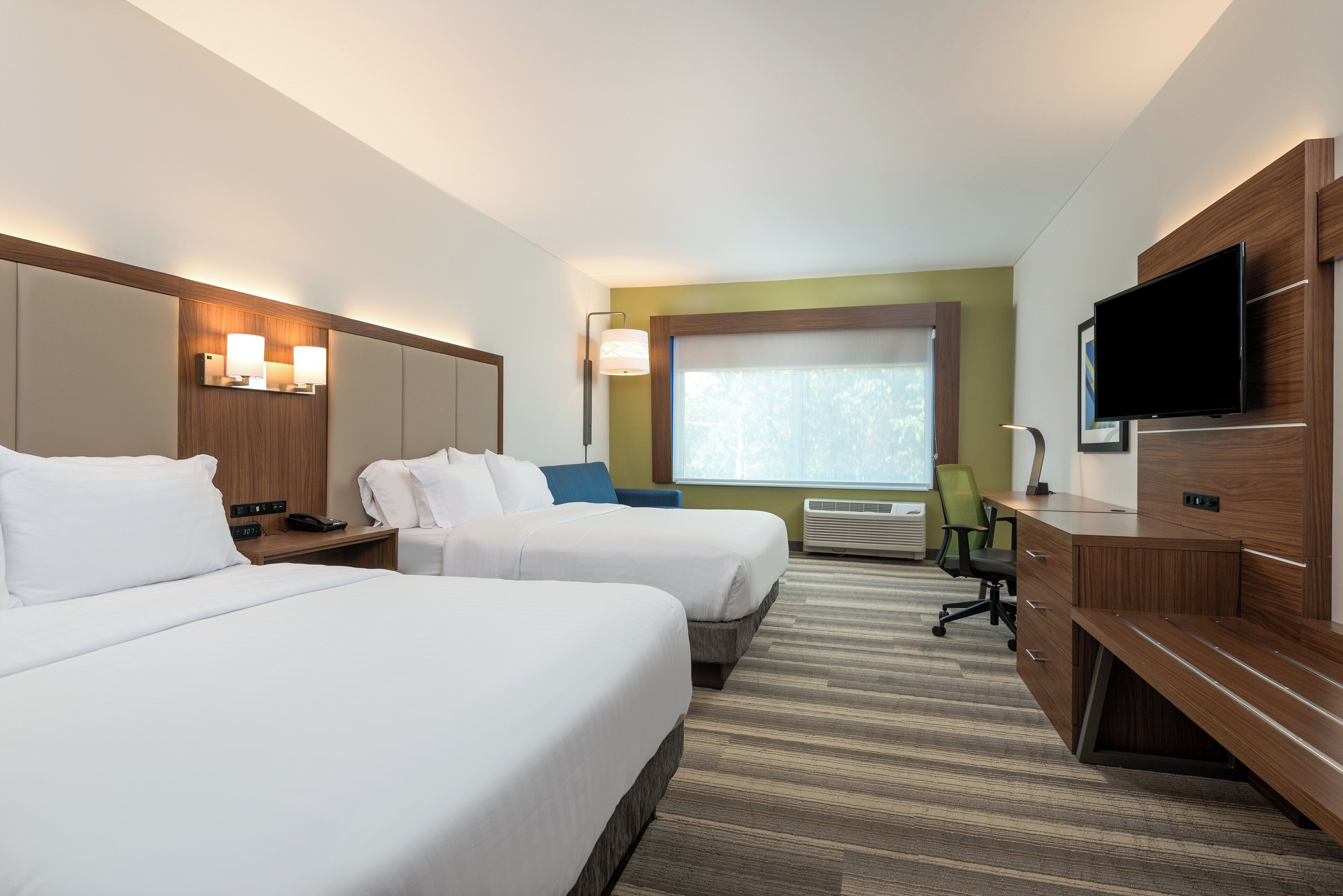Ein Hotelzimmer mit zwei Betten, einem Schreibtisch, einem Fernseher und einem Fenster mit Jalousien.