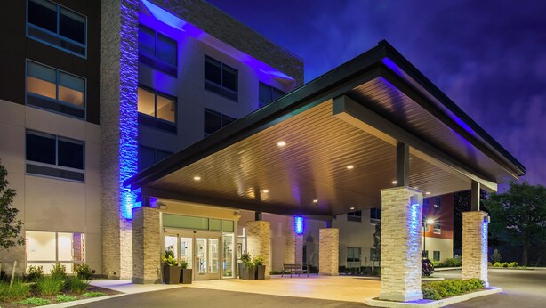 A modern hotel entrance with a covered waiting area, stone pillars, and a blue-lit facade.