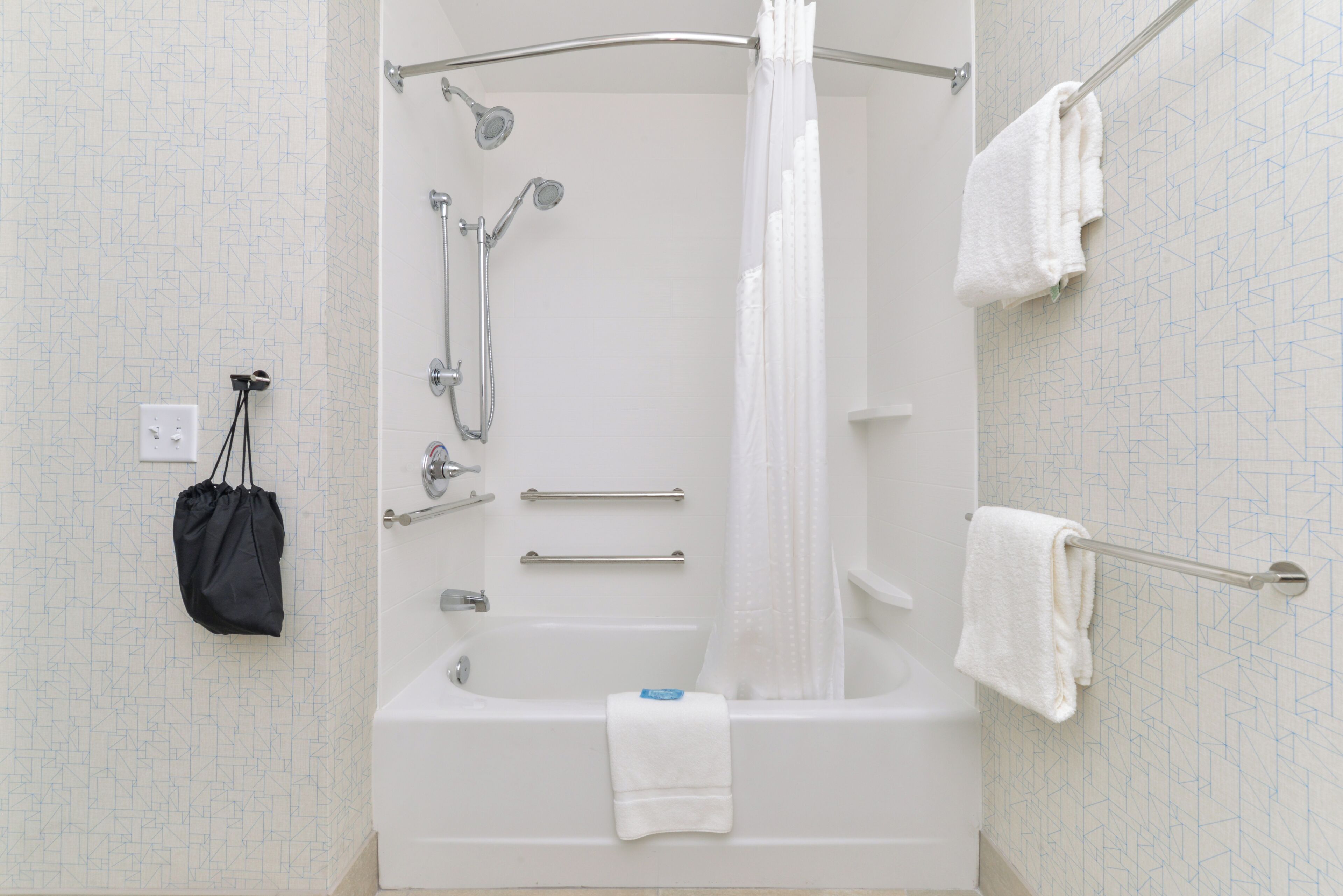 Une salle de bain moderne dotée d’une douche à l’italienne, de barres d’appui et d’un porte-serviettes.