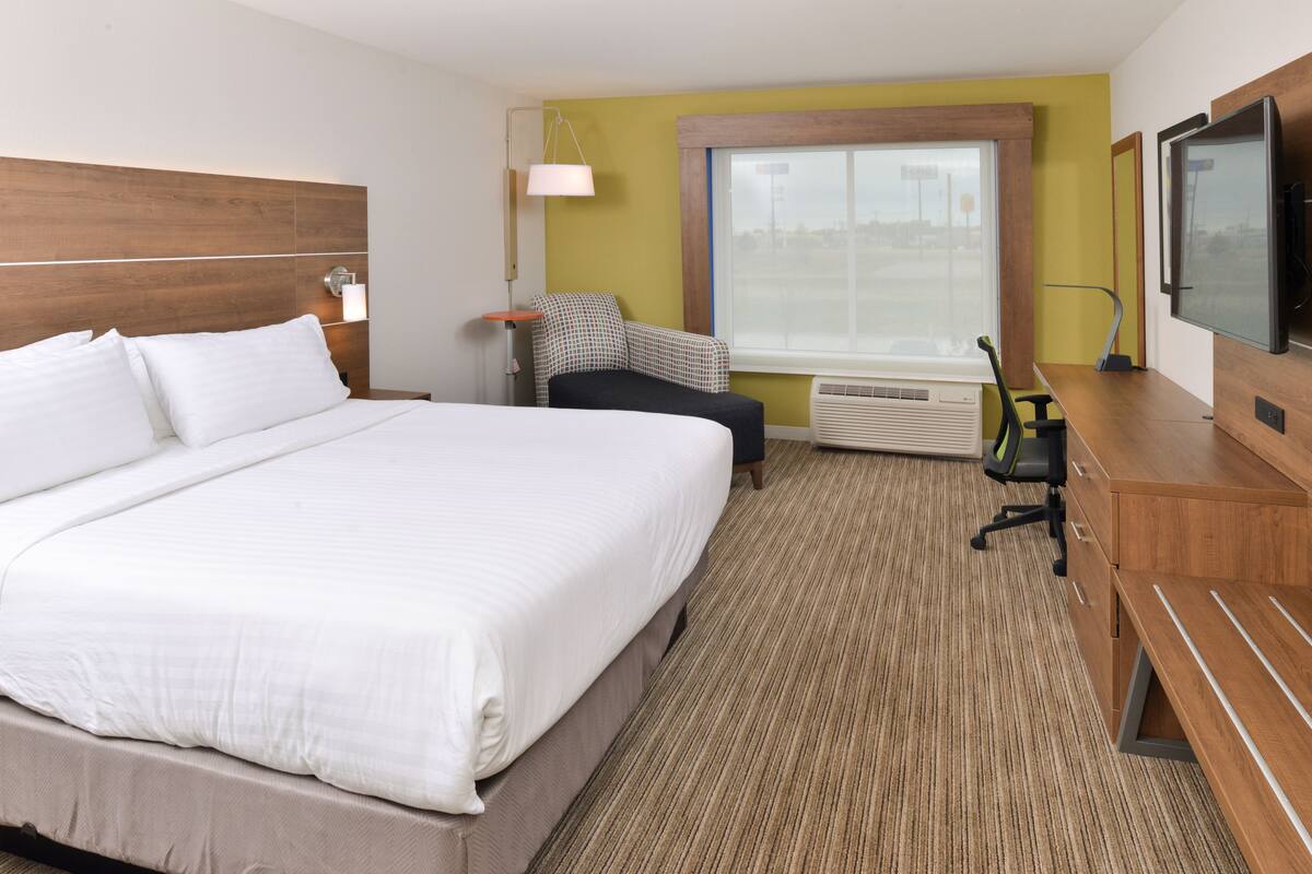 A hotel room with a large bed, a desk with a chair, a television, and a window with a view of the outside.
