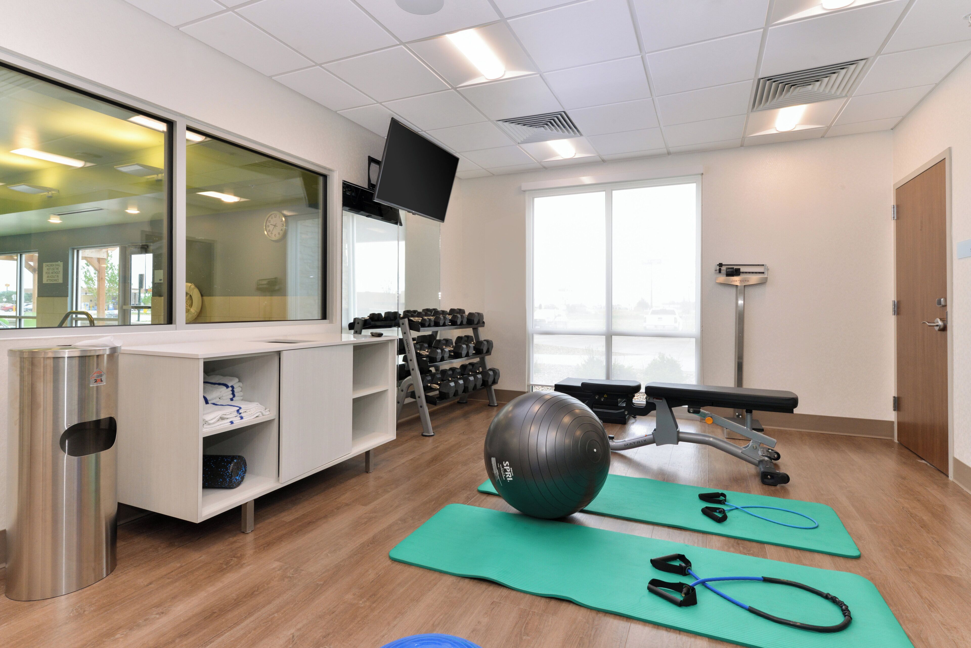 Un gimnasio con equipo de ejercicio, televisión y ventana.