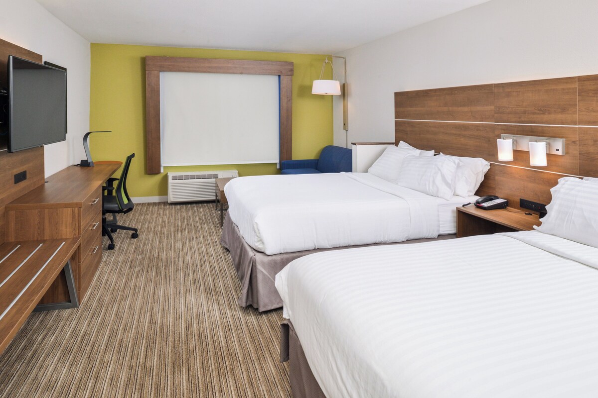 Une chambre d’hôtel avec deux lits, un bureau avec une chaise, une télévision et une grande fenêtre.