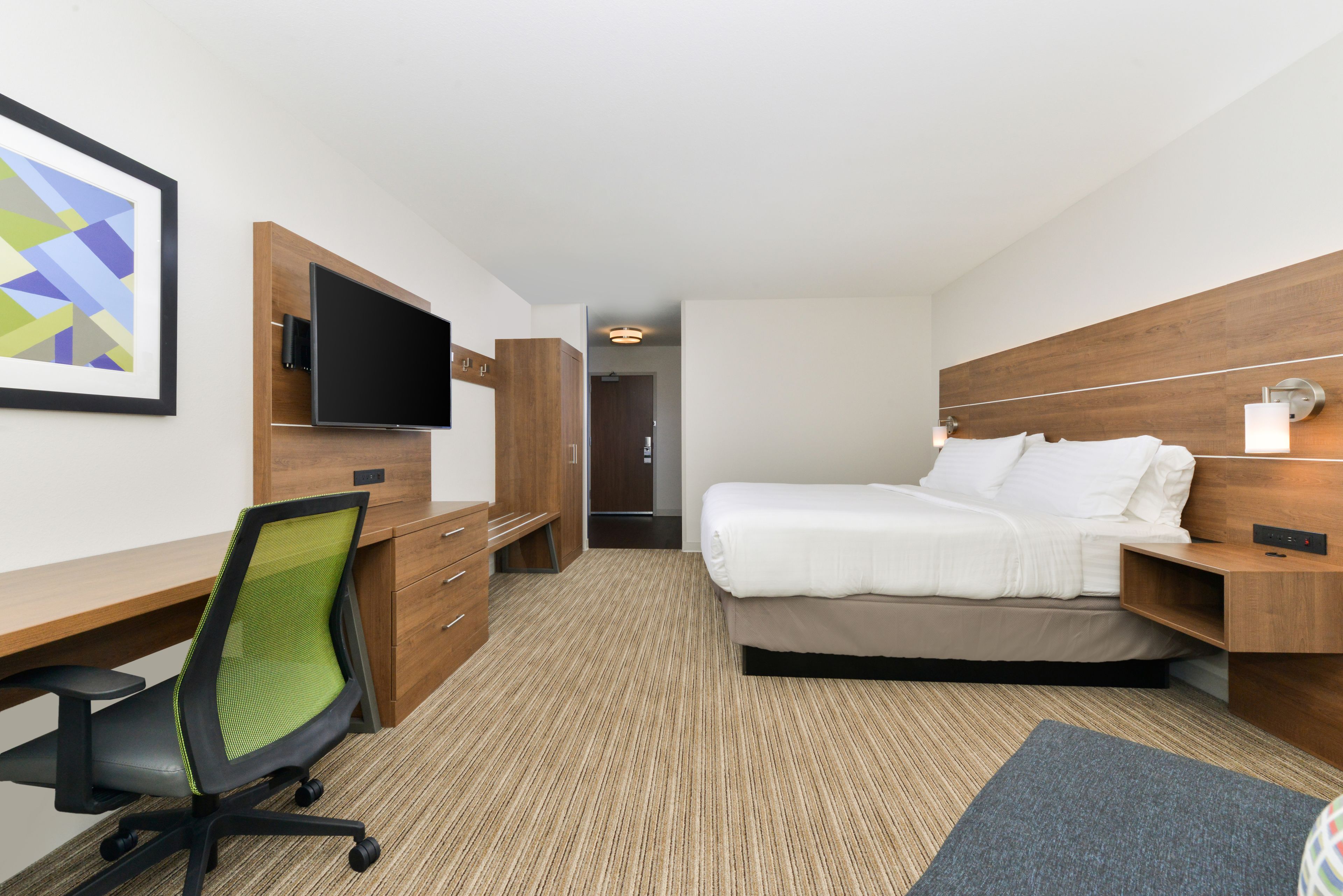 Habitación de hotel con cama, escritorio con silla, televisor y cabecero de madera.