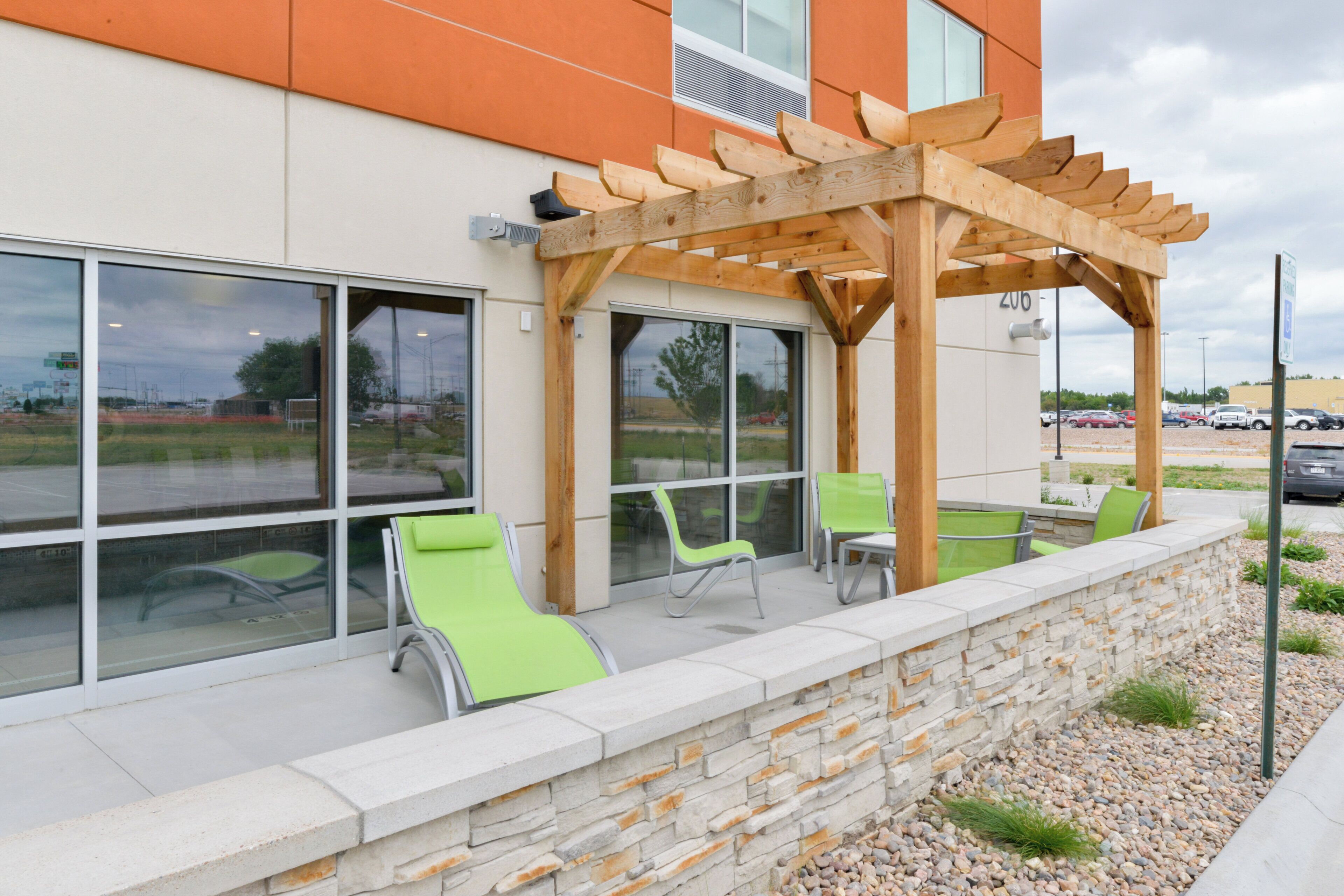 A building with a stone wall, outdoor seating with chairs, and a wooden pergola structure.