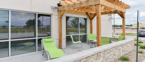 A building with a stone wall, outdoor seating with chairs, and a wooden pergola structure.