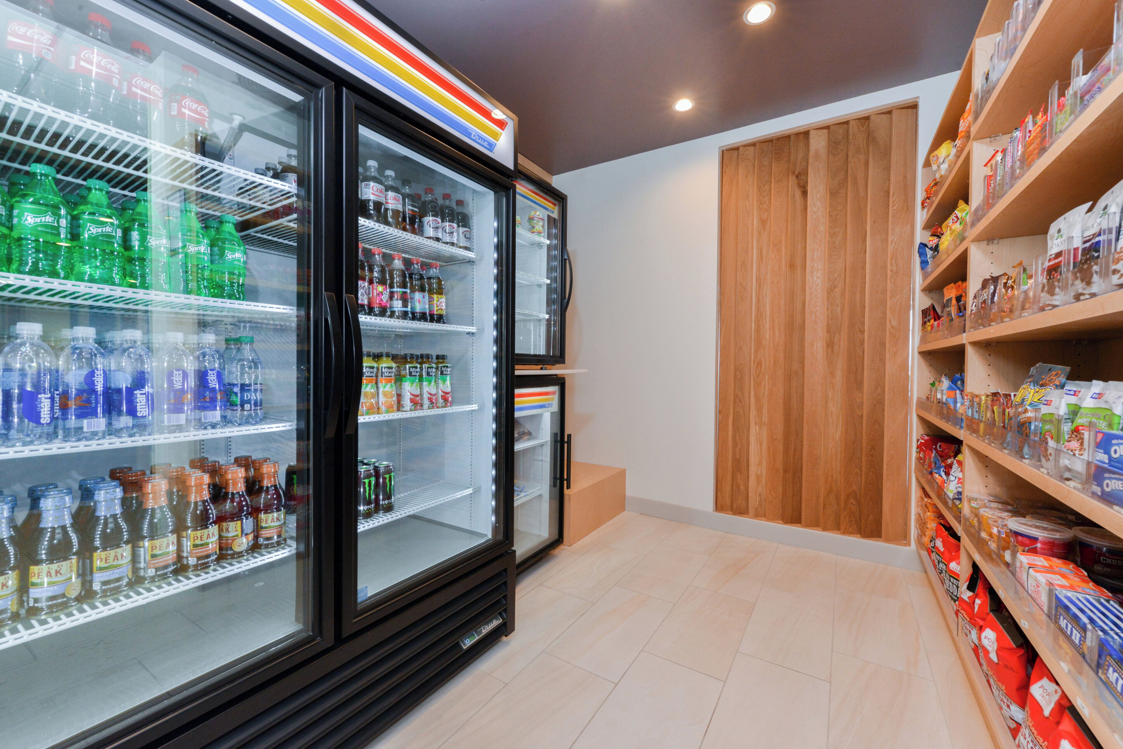 Un refrigerador exhibe diversas bebidas y una estantería contigua con aperitivos envasados.