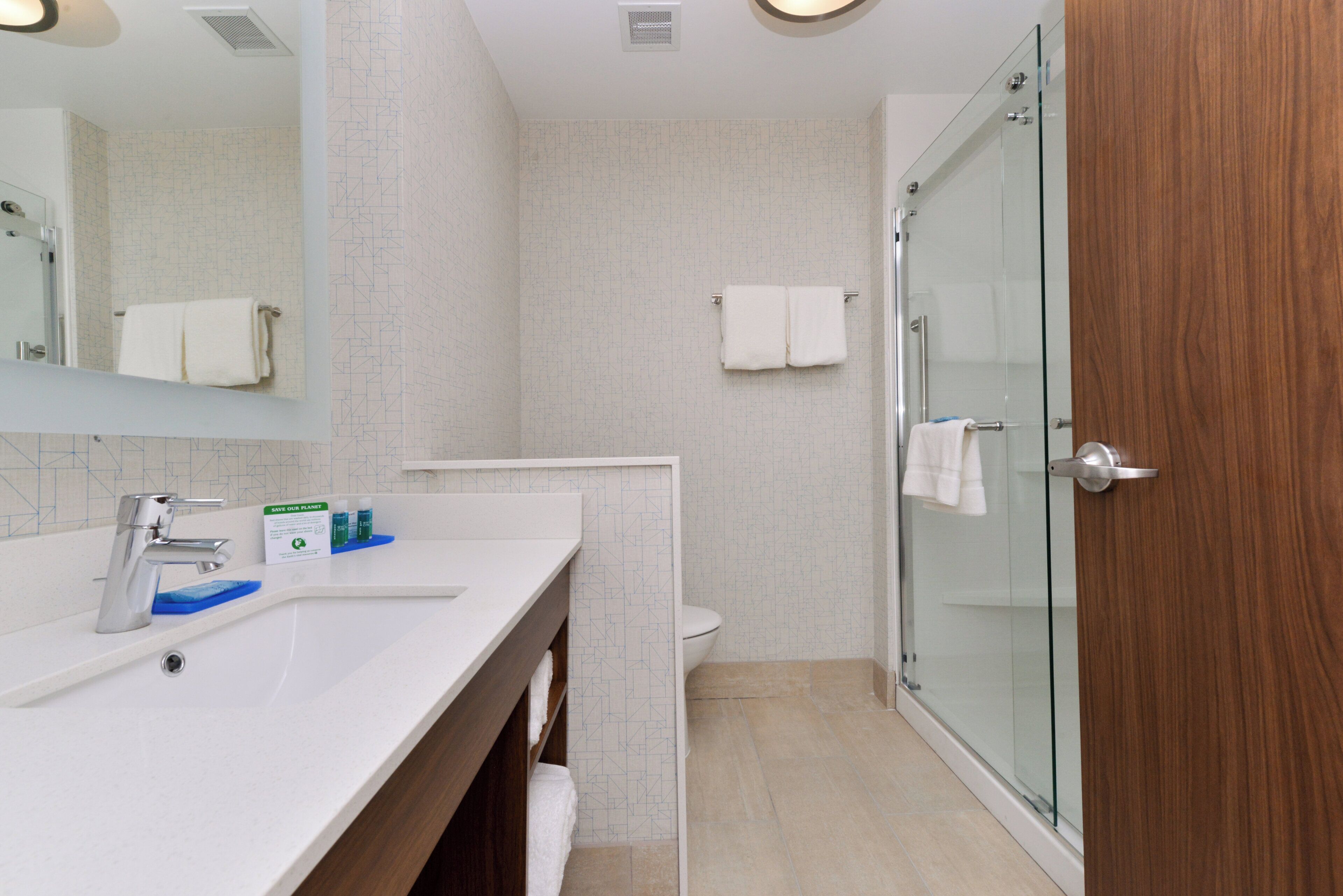 A modern bathroom with a white vanity, a glass shower enclosure, and a wooden door.