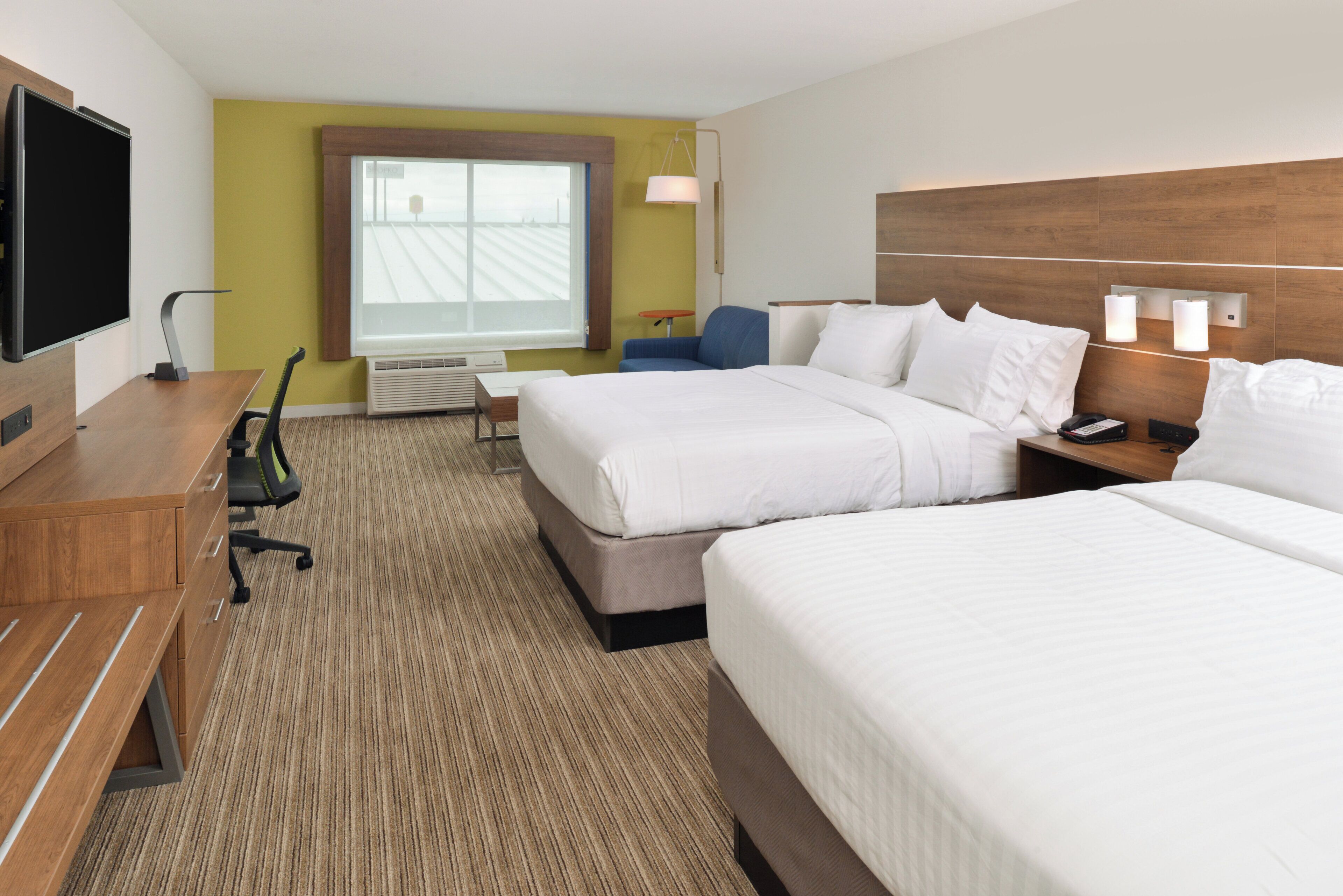 A hotel room with two beds, a desk, a chair, a TV, and a window with blinds.