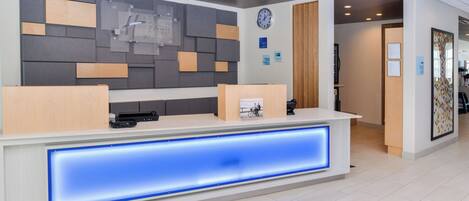 A hotel reception desk with a modern design, a clock, and a sign indicating check-in and check-out times.