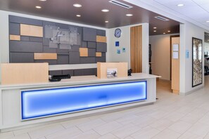 Un comptoir d’accueil d’hôtel au design moderne, avec une horloge et un panneau indiquant les heures d’arrivée et de départ.