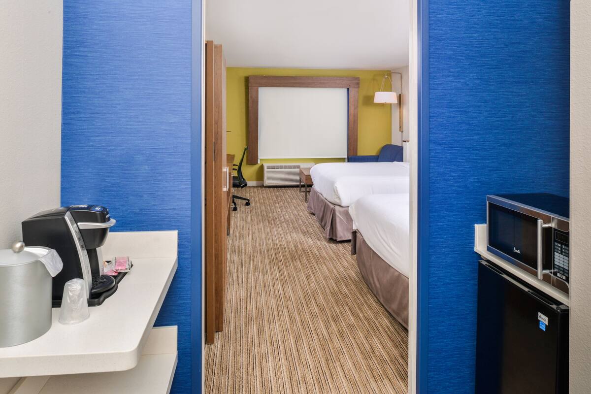 A hotel room with a bed, a desk with a coffee maker, a TV, and a microwave.