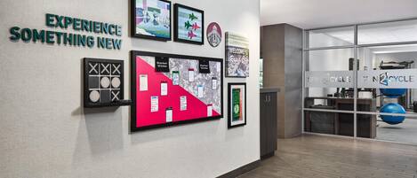 A modern interior with a wall-mounted display of framed pictures and text, a reception area with a glass door, and a visible exercise ball.