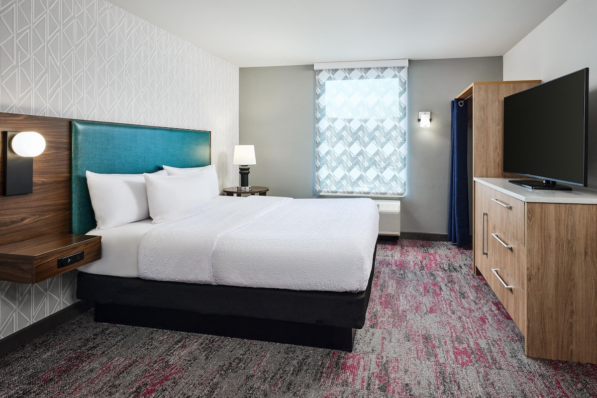 A hotel room with a bed, a TV, a desk, and a window with a view.