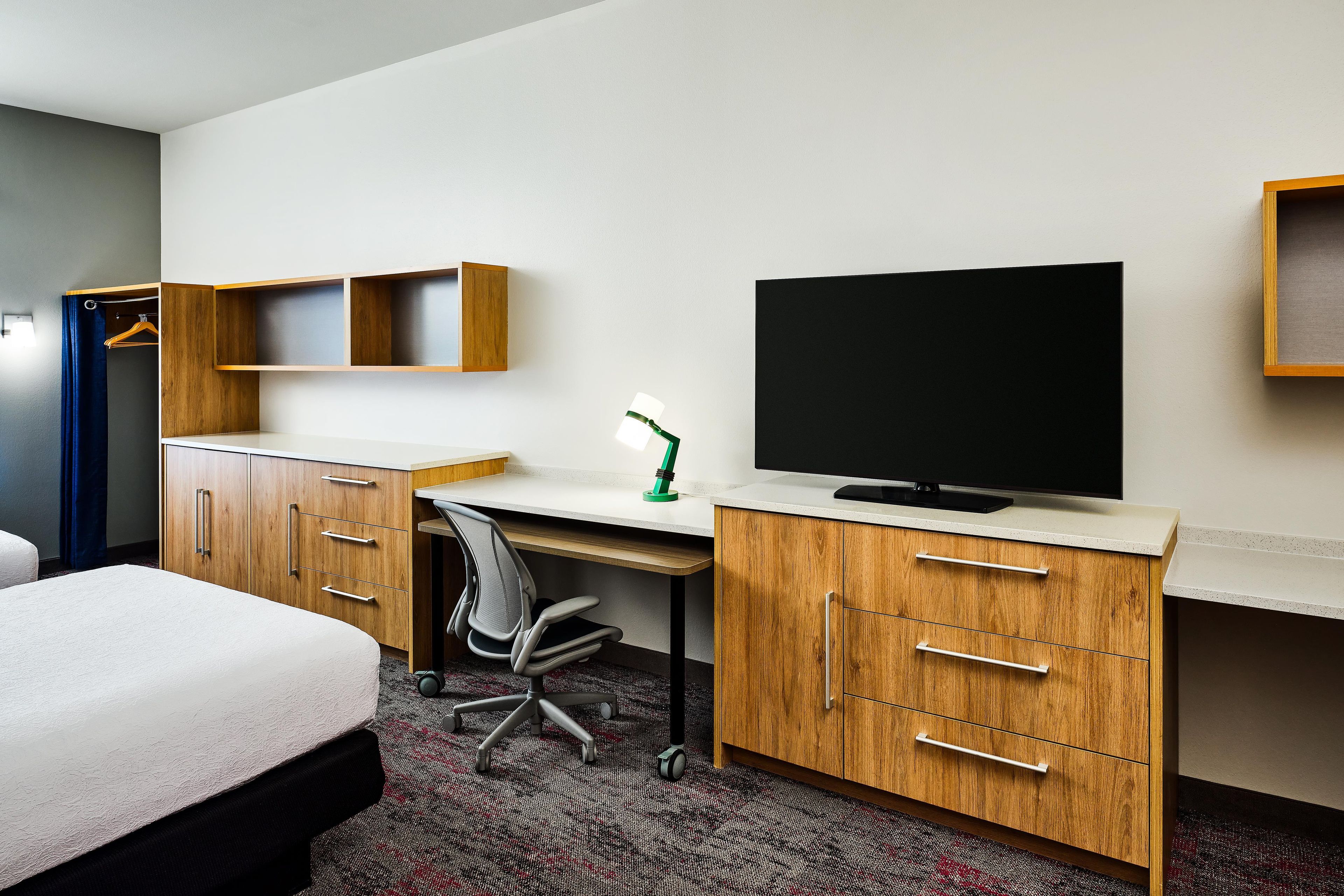 A hotel room with a bed, a desk with a chair, a television, and a wardrobe.