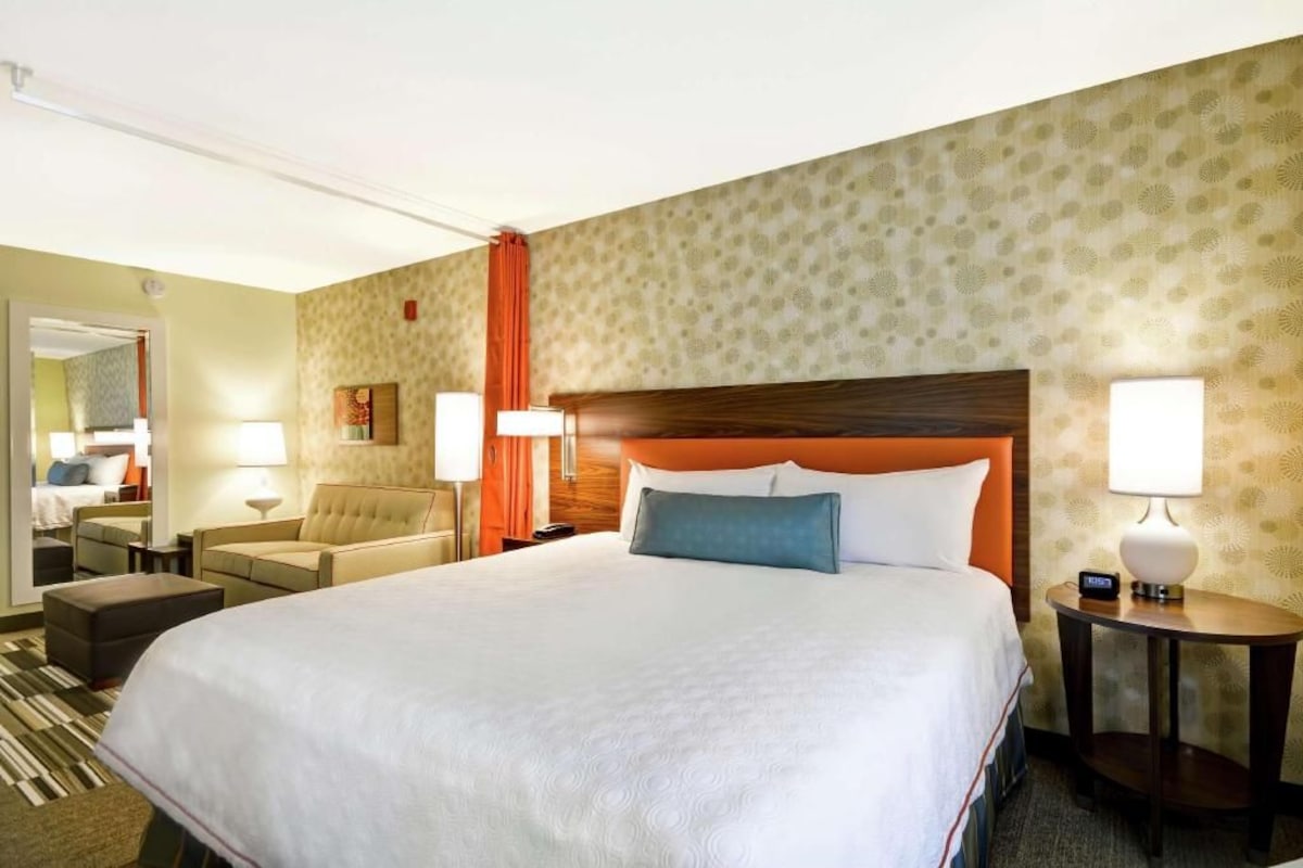 A hotel room with a large bed, a sofa, a desk, and a mirror.