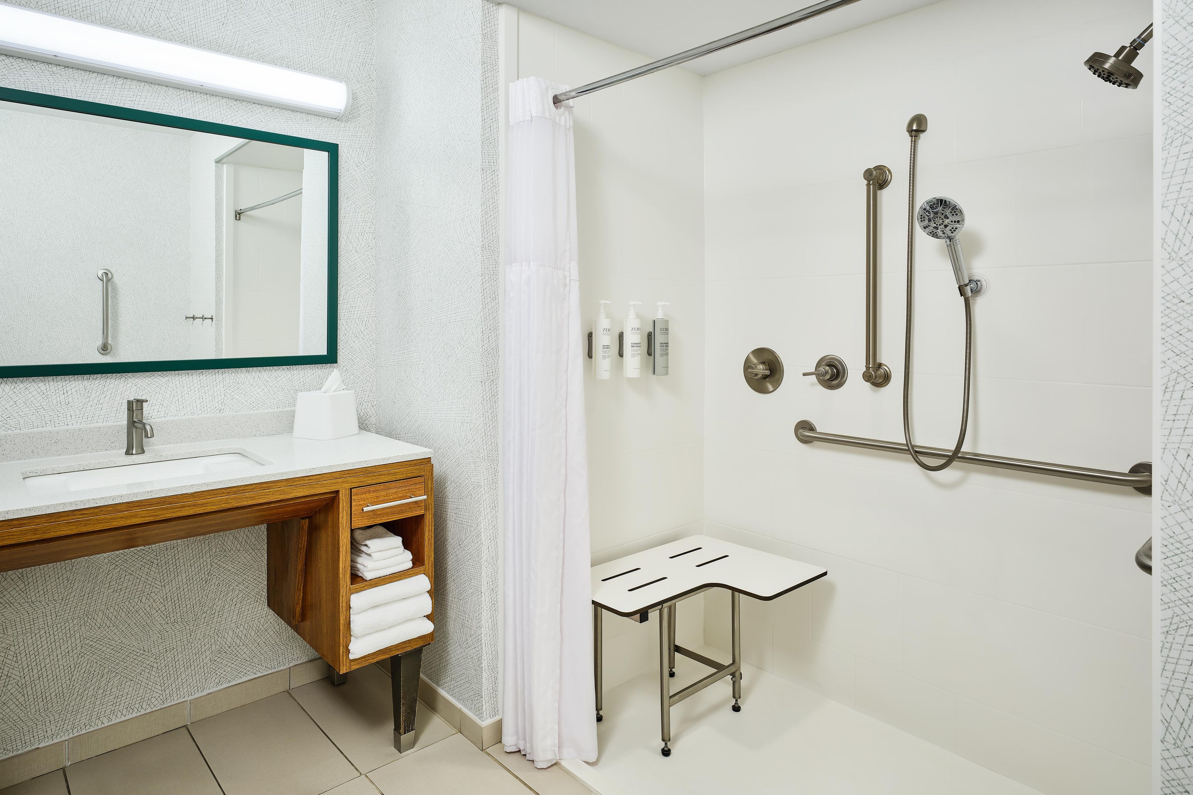 A modern bathroom with a shower, a vanity with a mirror, and a small stool.