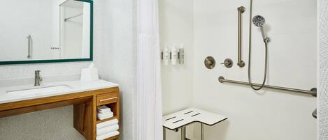 Een moderne badkamer met een douche, een wastafel met spiegel, en een klein krukje.