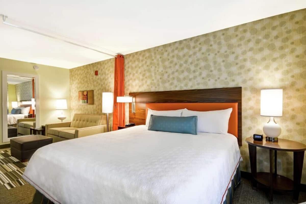 A hotel room with a large bed, a sofa, a desk, and a mirror.