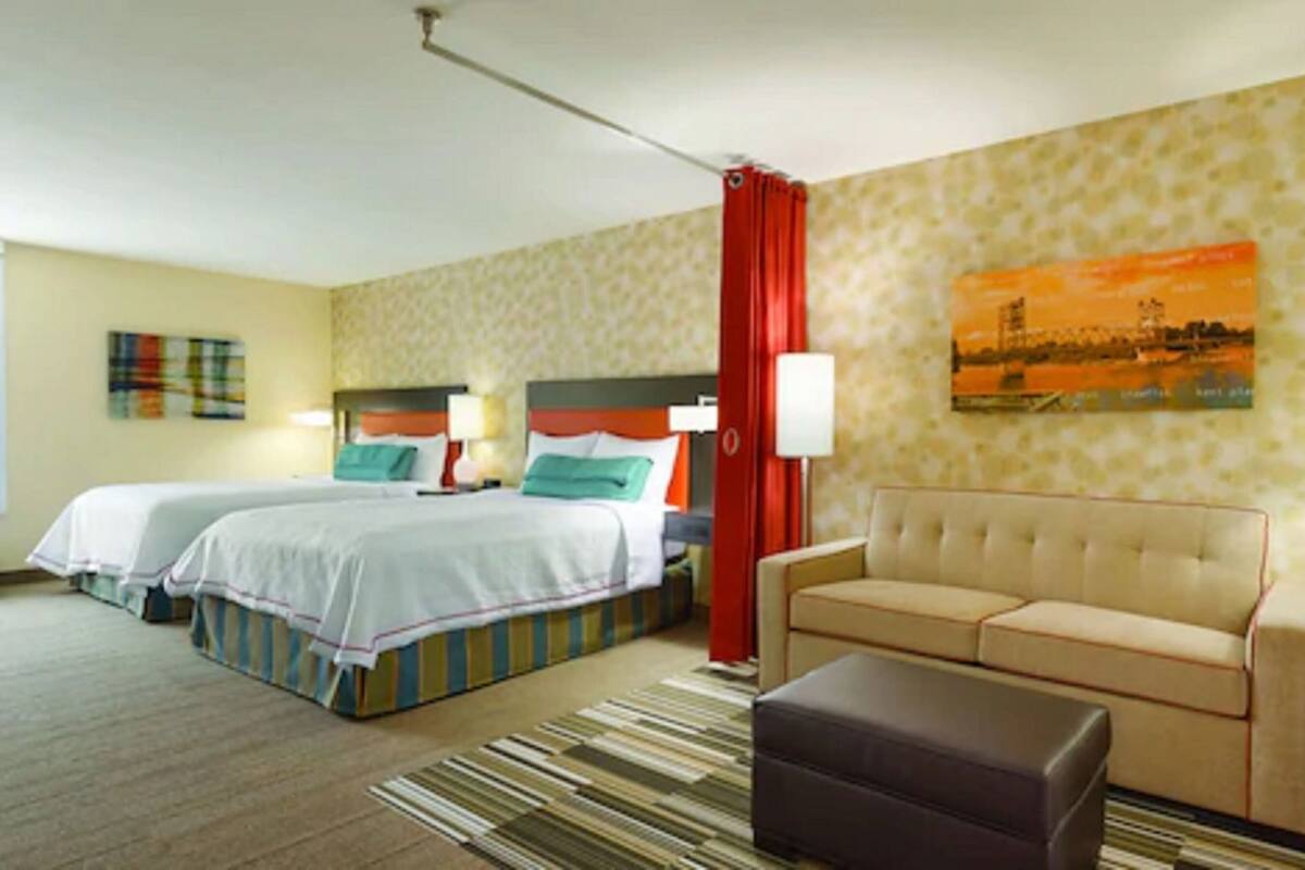 A hotel room with two beds, a sofa, a chair, a lamp, and a painting on the wall.