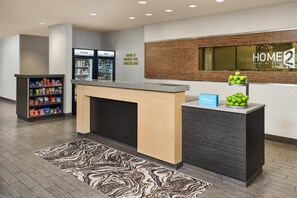 A hotel reception area with a counter, a minibar, and a wall-mounted sign. - Home2 Suites by Hilton Rapid City (Rapid City)