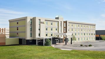 A multi-story hotel with a central entrance, a covered parking area, and a well-maintained lawn.
