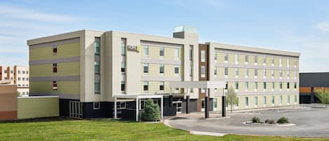 A multi-story hotel with a central entrance, a covered parking area, and a well-maintained lawn.