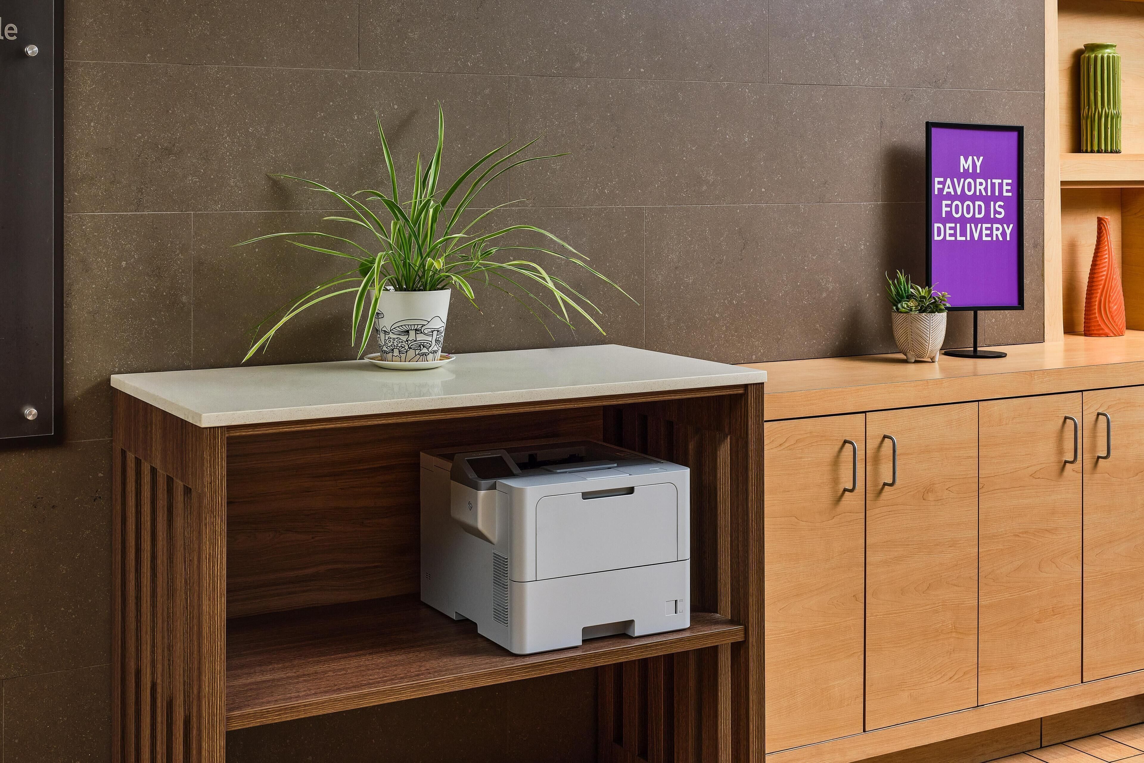 A kitchen area with a countertop, a printer, a potted plant, and a sign on the wall.