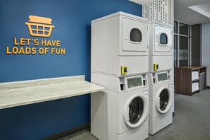 A laundry area with stacked washing machines and a shelf. - Home2 Suites by Hilton Rapid City (Rapid City)