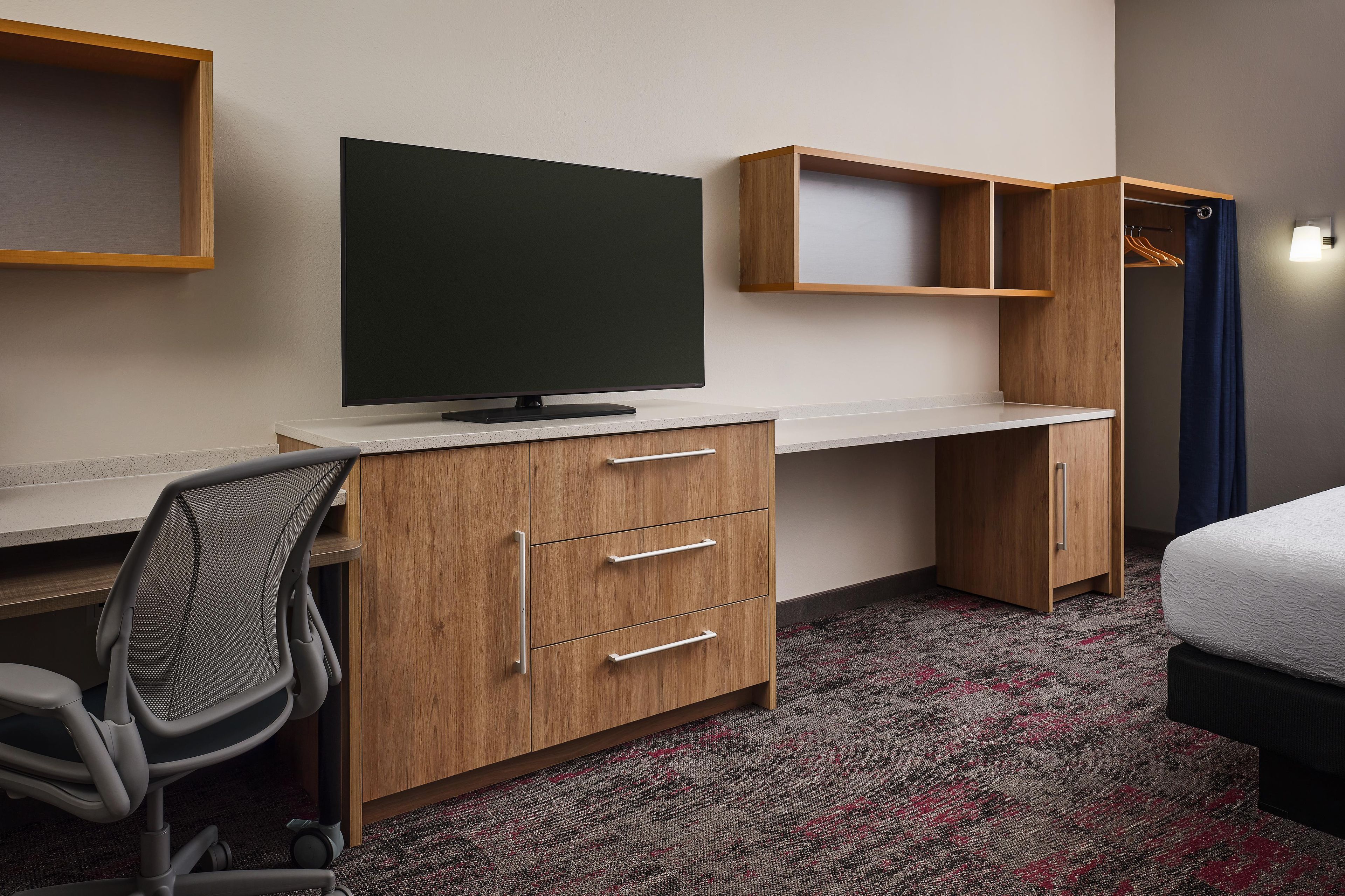 Ein Hotelzimmer mit Schreibtisch, Fernseher, Kleiderschrank und Bett.