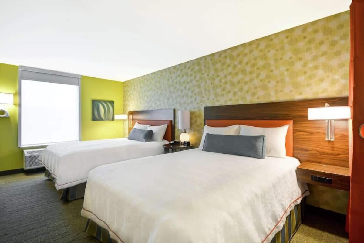 A hotel room with two beds, a window, and a wall with a patterned wallpaper.