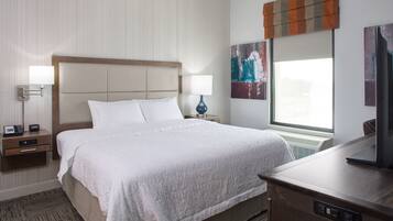 A hotel room with a large bed, bedside lamps, a desk with a TV, and artwork on the walls.