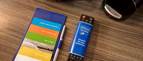 A notebook with a travel-themed cover, a pen, a remote control, and a black object on a wooden surface.