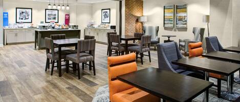 A modern hotel lobby with a dining area, kitchen, and seating arrangements.