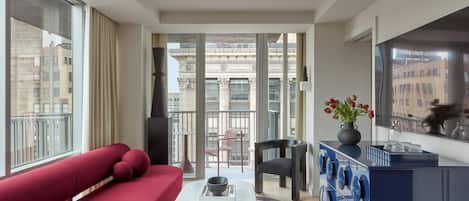 A modern living room with a red sofa, a coffee table with a book, a blue cabinet, and a view of a building through large windows.