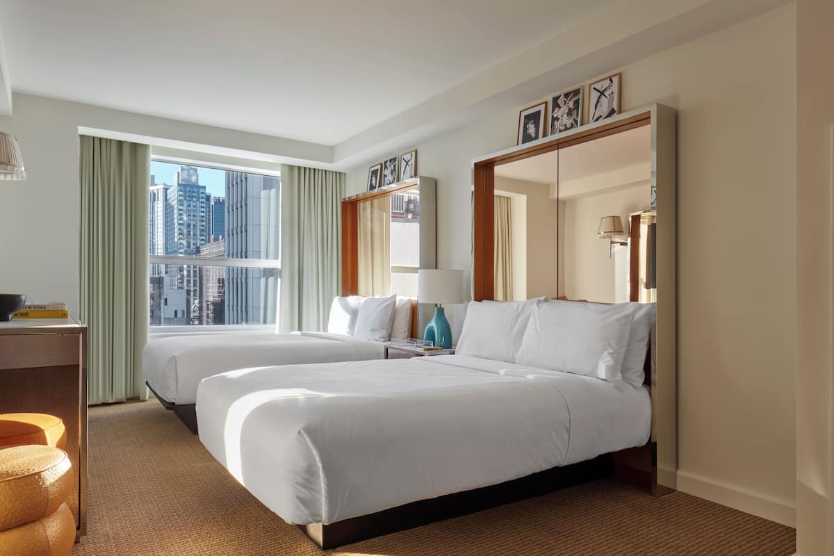 Habitación de hotel con dos camas, un escritorio, una lámpara y vistas a la ciudad.