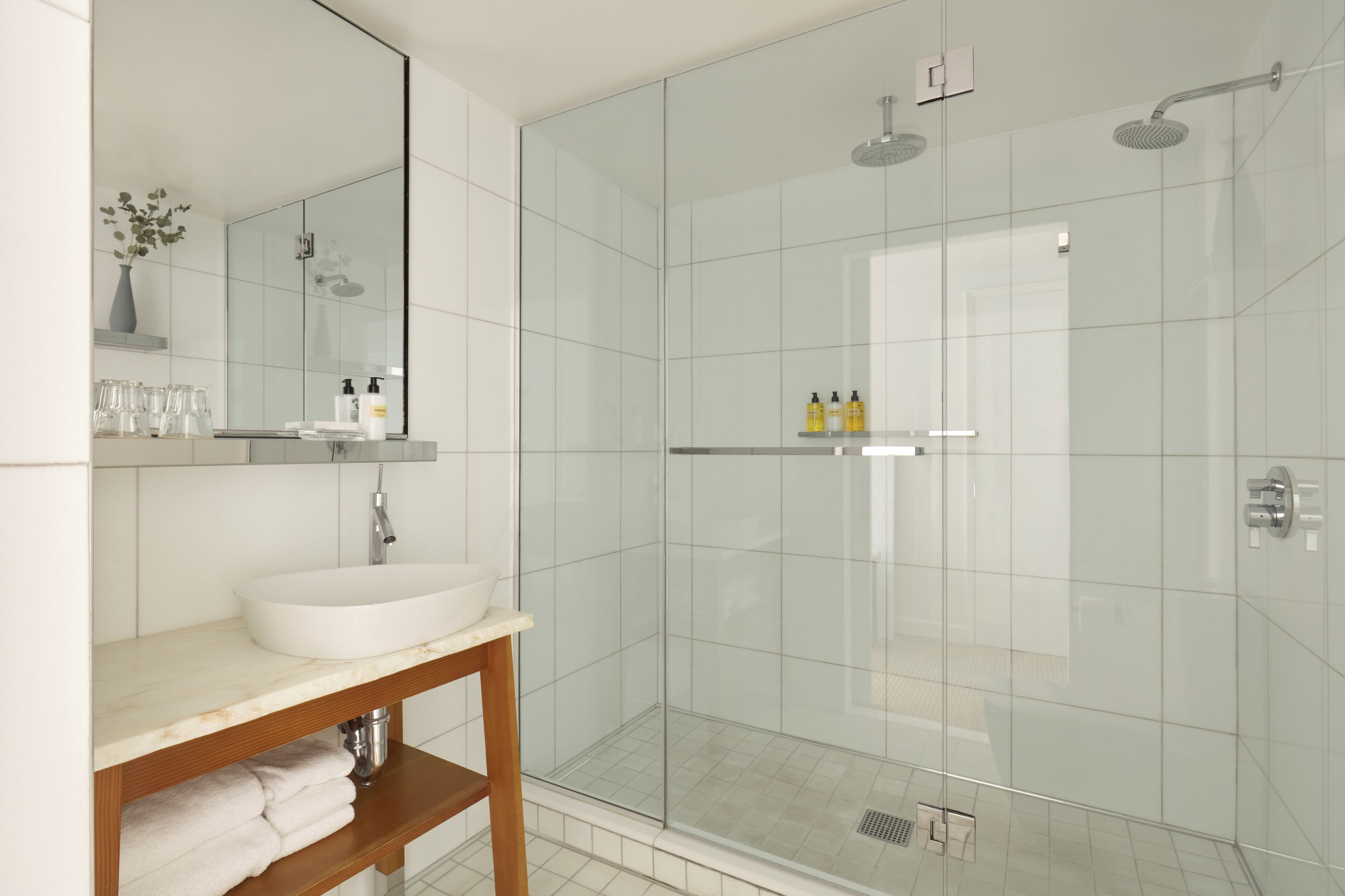 Ein modernes Badezimmer mit einer gläsernen Duschkabine, einem weißen Waschbecken und einem Spiegel darüber.