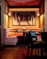 A cozy restaurant with a booth seating arrangement, a table set for dining, and a wall adorned with hanging plants.