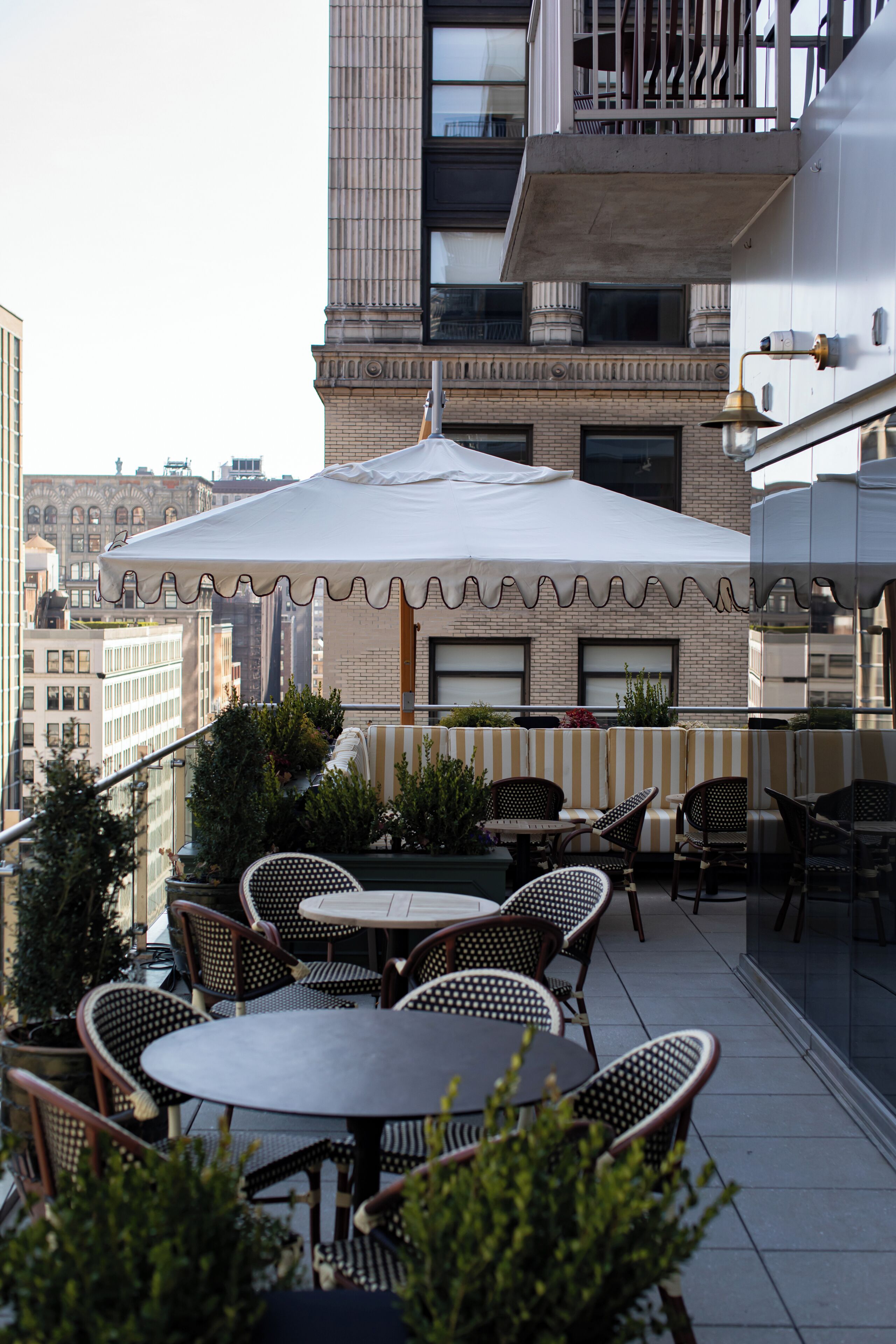 An outdoor seating area with tables and chairs, a white umbrella, and a view of the cityscape.