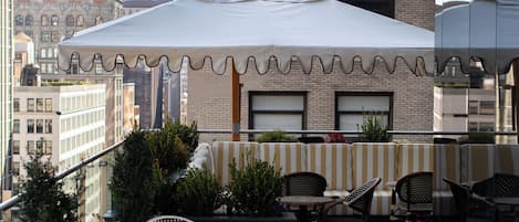 An outdoor seating area with tables and chairs, a white umbrella, and a view of the cityscape.