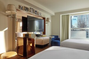 Hotelkamer met een bed, een bureau met een flatscreen-televisie, een stoel en een raam met uitzicht op gebouwen.