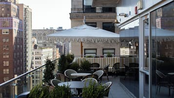 Terraza exterior con mesas, sillas y sombrillas, con vista a un paisaje urbano con edificios.