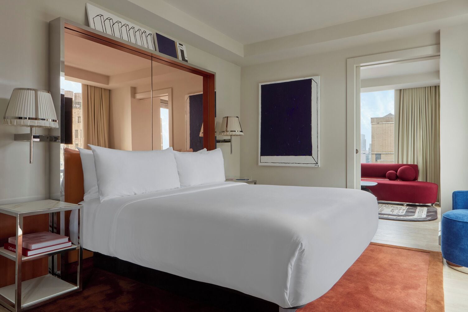 A hotel room with a large bed, a red sofa, a blue armchair, and a view of the city.